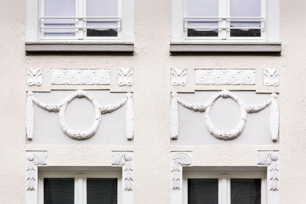 Detail-Darstellung einer mit Stuck verzierten Altbaufassade mit Fenstern