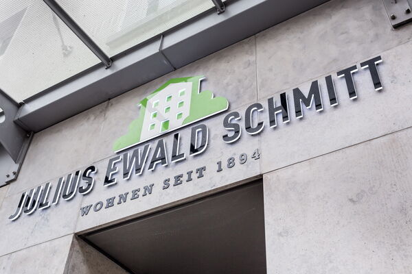 Metallisches Firmenschild mit Logo und Schriftzug Julius Ewald Schmitt an einer Steinfassade über einem Gebäudeeingang.