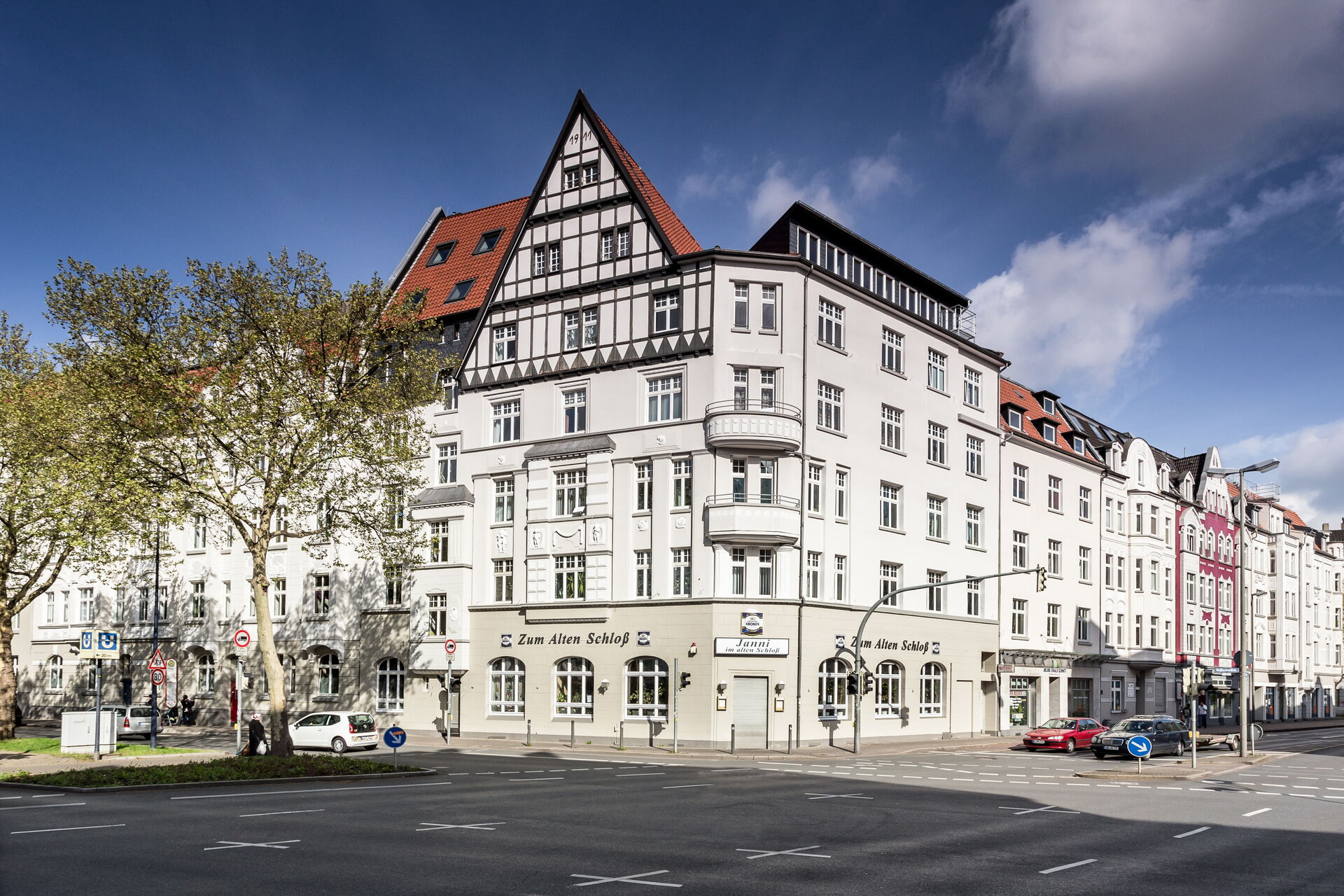 Mehrstöckiges historisches Gebäude mit Fachwerkgiebel und heller Fassade an einer Straßenkreuzung in einer innerstädtischen Umgebung.