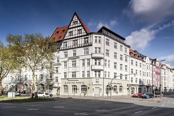 Mehrstöckiges historisches Gebäude mit Fachwerkgiebel und heller Fassade an einer Straßenkreuzung in einer innerstädtischen Umgebung.
