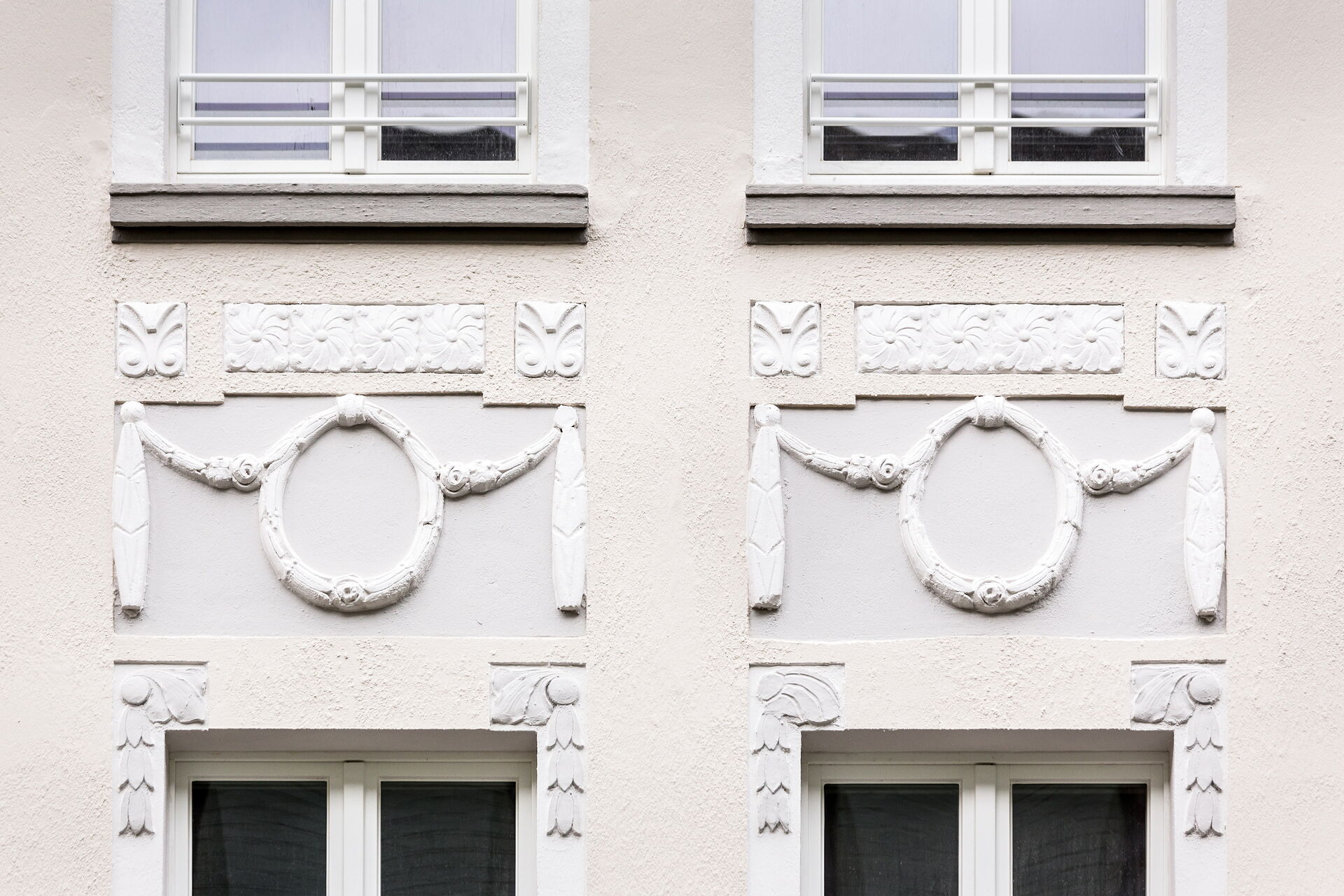 Detail-Darstellung einer mit Stuck verzierten Altbaufassade mit Fenstern